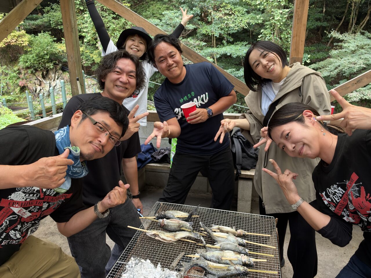 釣ったマスを焼くBBQコンロを囲んで笑顔で写真を撮るスタッフたち